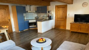 A modern kitchen with blue cabinets, a central island, and a dining area with a round table and sofas. - Apartment 'Haus Peschl Fewo 1' with Shared Terrace, Shared Garden and Wi-Fi (Neureichenau)