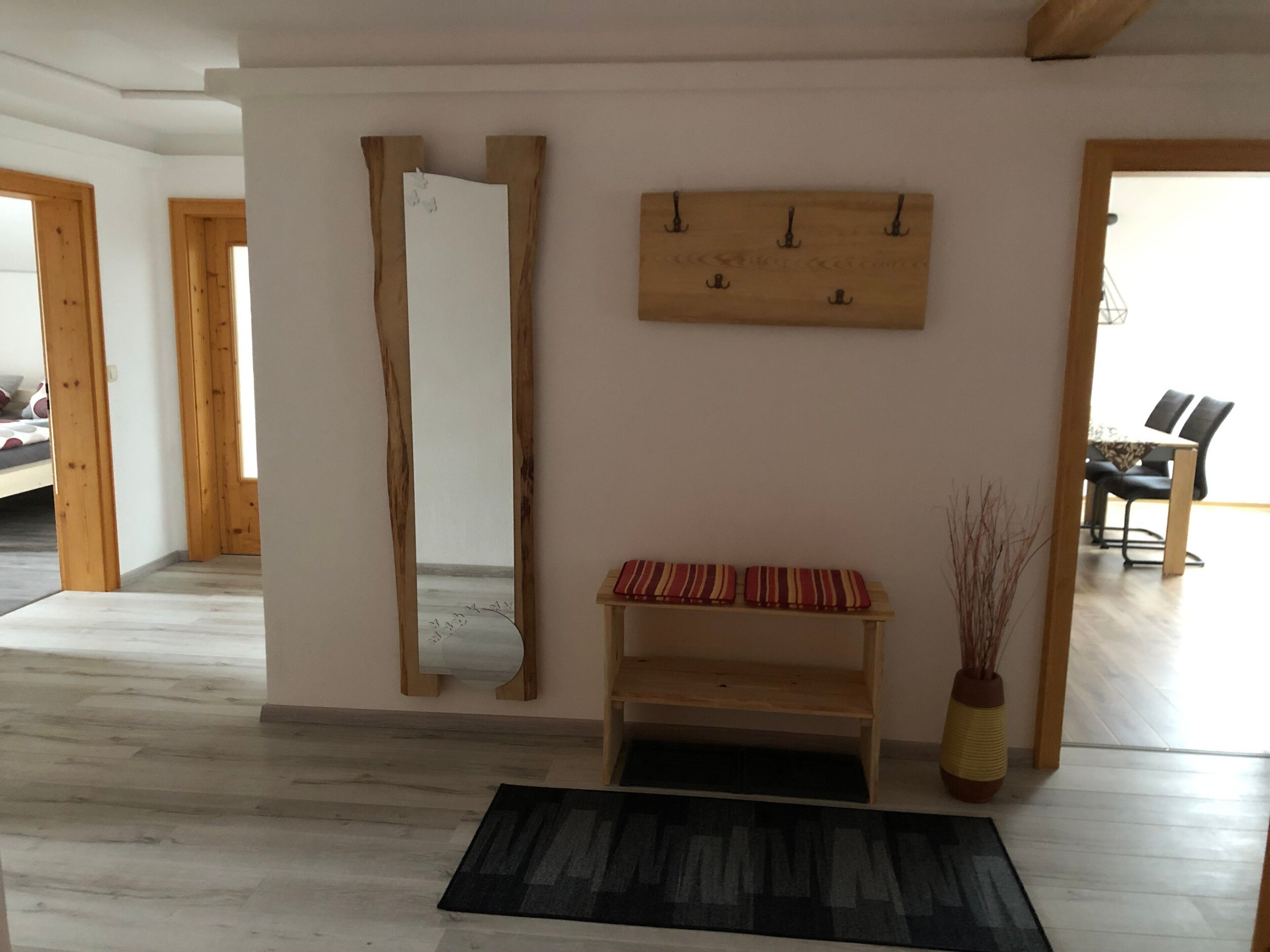 A room with a wooden bench, a mirror, and a wall-mounted shelf.