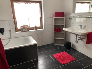 Une salle de bain avec une baignoire, un lavabo, une fenêtre et un tapis rouge.
