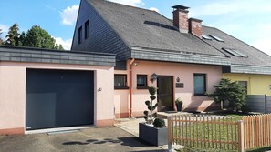 A two-story house with a garage, a small front porch, and a fenced yard. - Holiday Home 'Am Ring' with Private Terrace, Private Garden and Wi-Fi (Spielberg)