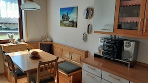 A dining area with a wooden table and chairs, a bench, a window with a view, a painting, and a vintage radio. - Holiday Home 'Am Ring' with Private Terrace, Private Garden and Wi-Fi (Spielberg)
