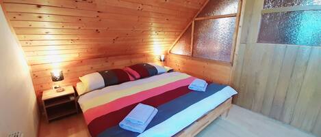Una habitación con techo inclinado, una cama con ropa de cama a rayas, dos lámparas de noche y un ventanal con vidrio esmerilado.
