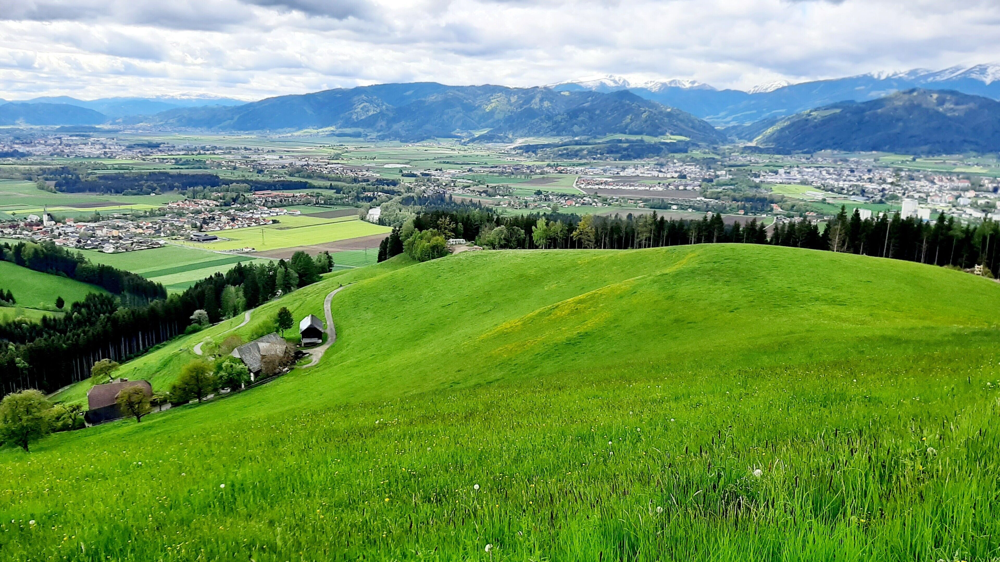 Vista panorámica de un valle verde con un pueblo a lo lejos, rodeado de montañas.