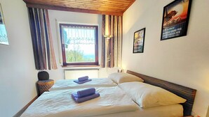 Un lit double avec des oreillers et des serviettes, une table de chevet avec une lampe, une fenêtre avec des rideaux et une affiche accrochée au mur.