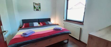 Une chambre à coucher avec un lit, un radiateur, une fenêtre et une porte.