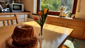 Une cuisine avec un gâteau en forme de couronne sur une assiette, un vase rempli de fleurs et une fenêtre donnant sur des arbres.