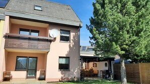 Une maison à deux étages avec un balcon, une antenne parabolique et un arbre dans la cour.