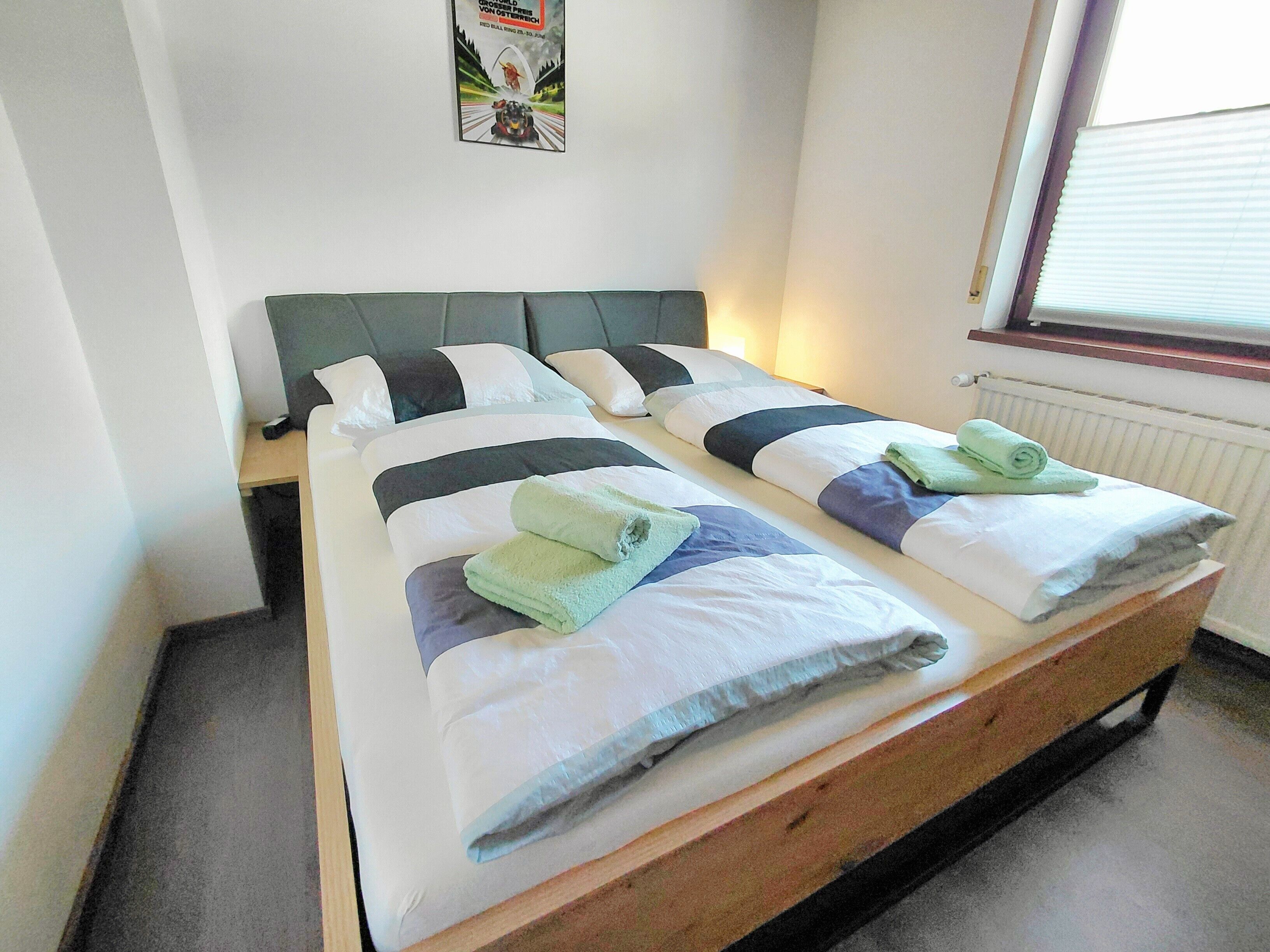 Ein Doppelbett mit zwei Kissen, einem Kopfteil und einem Nachttisch mit Lampe.