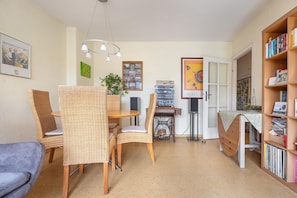 A cozy room with wicker furniture, a dining table, a bookshelf, and a sewing machine.