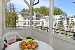 A balcony with a table holding a fruit bowl, a white chair, and a view of historic buildings.