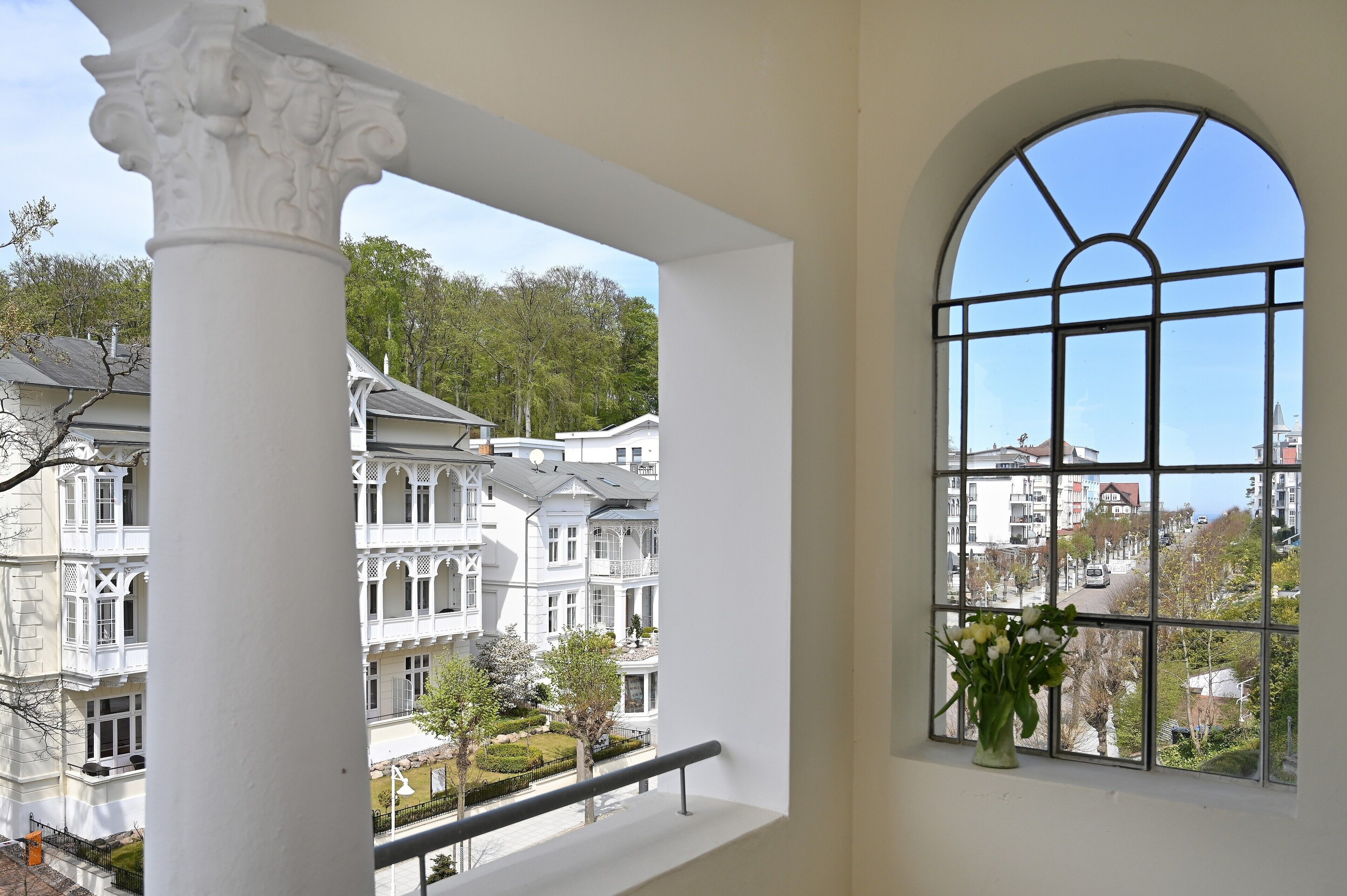 Ein Zimmer mit einem großen Bogenfenster, einer weißen Säule und Blick auf mehrstöckige Gebäude.