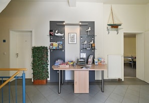 A room with a desk, shelves with books and decorative items, a potted plant, and a small cabinet.