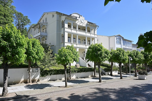 A building with a balcony, a sign reading 'Villa Colosio,' and a paved walkway with trees.