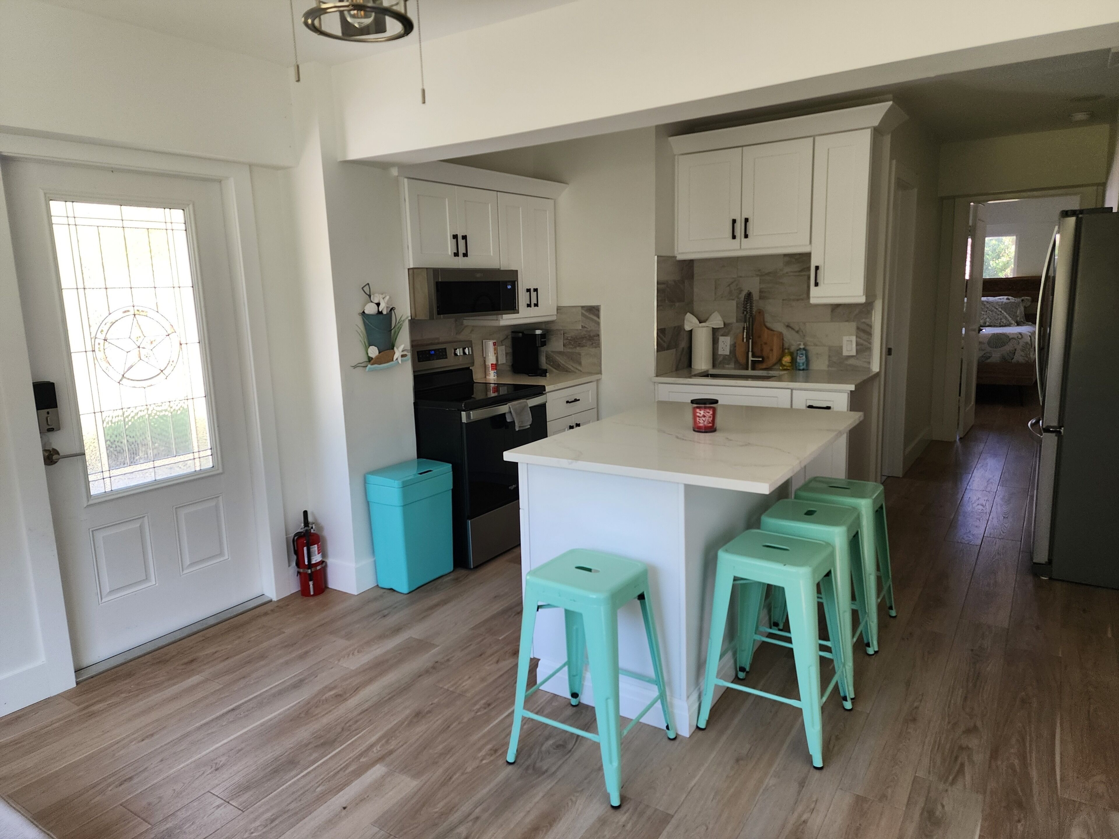 A modern kitchen with white cabinets, a black stove, and a teal trash bin. There are three teal stools at the island.