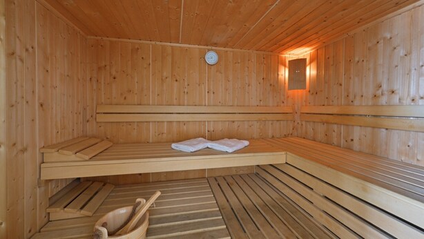 A wooden sauna with benches, a clock, and a towel rack.