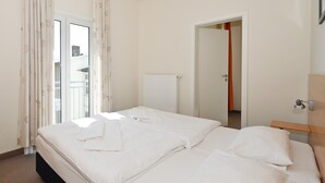 A hotel room with a bed, a radiator, a door, and a window with curtains.