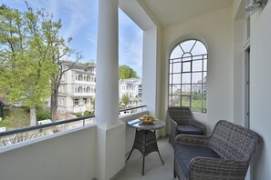 En balkon med fletningsmøbler, et bord med frugt og udsigt til historiske bygninger.