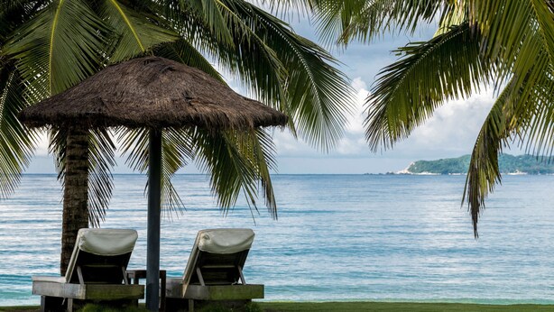 A beach with a thatched umbrella and two lounge chairs. - Anyu Hotel Sanya (Sanya)