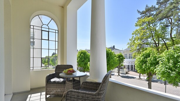 Ein Balkon mit Korbmöbeln, einem runden Tisch und einer Obstschale.