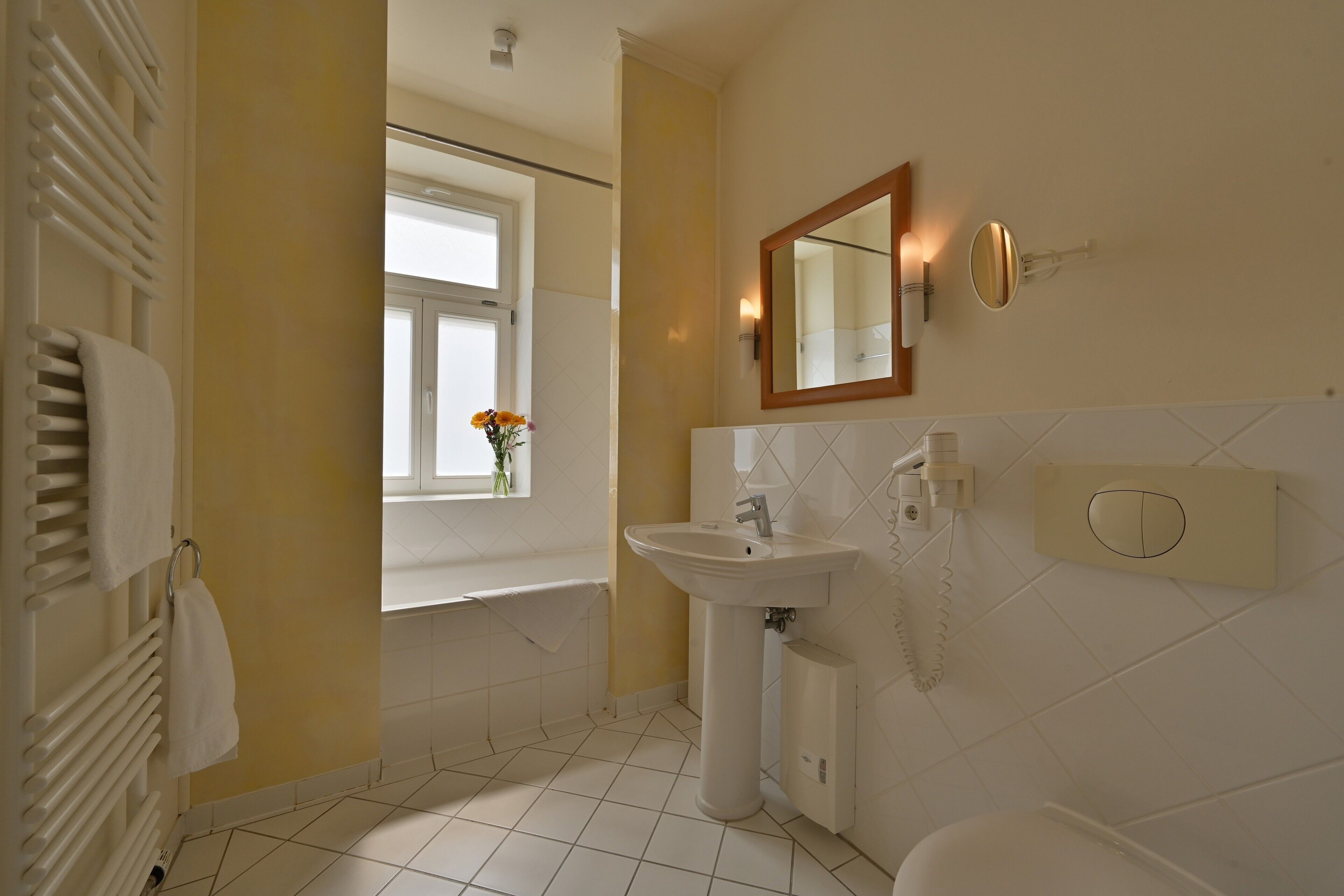 A bathroom with a white sink, a mirror, a towel rack, and a window with flowers.
