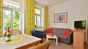 Ein möblierter Raum mit Esstisch, Stühlen, einer Couch, einem Fernseher und einem kleinen Tisch mit Obst.