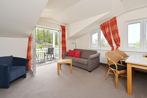 A room with a sofa, a chair, a table, and a balcony with a view of trees.