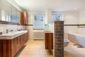 Un baño moderno con tocador, inodoro, bañera y ventana con vista a árboles.