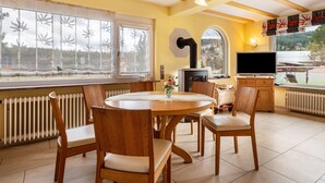 A dining area with a round table, wooden chairs, a TV, and a view through large windows. - Holiday Home 'Ferienhaus Schwarzwälder Kirsch' with Private Terrace, Balcony and Wi-Fi (Feldberg)