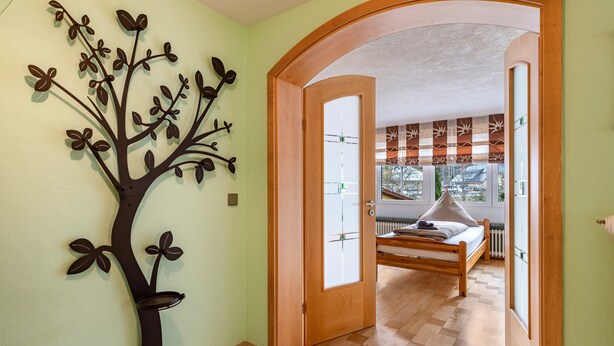 A bedroom with a bed, a wooden door, and a wall-mounted tree decoration. - Holiday Home 'Ferienhaus Schwarzwälder Kirsch' with Private Terrace, Balcony and Wi-Fi (Feldberg)