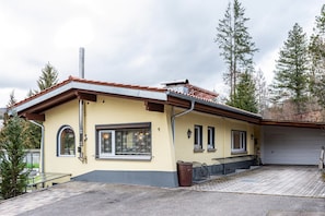 Une maison à deux étages avec un garage, une véranda et un petit espace extérieur aménagé pour s’asseoir.