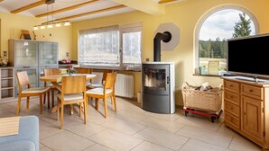 A cozy living room with a dining area, a fireplace, a television, and a large window with a view of trees. - Holiday Home 'Ferienhaus Schwarzwälder Kirsch' with Private Terrace, Balcony and Wi-Fi (Feldberg)