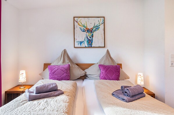 Un lit double avec une tête de lit, deux oreillers, une couverture et une serviette enroulée. Une œuvre d’art est accrochée au mur au-dessus du lit.