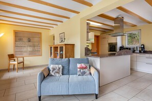 Une cuisine moderne dotée d’un îlot central, de poutres en bois au plafond et d’un canapé agrémenté de coussins décoratifs.