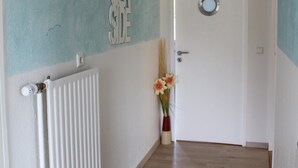Un couloir avec un radiateur, une porte dotée d’une poignée ronde et un mur sur lequel est affiché un panneau indiquant « CÔTÉ MER ».