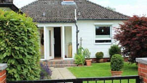Une maison avec un toit en tuiles, une porte d’entrée et un petit jardin agrémenté de plantes en pot.