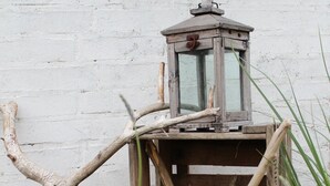 Une lanterne rustique dotée d’un cadre en bois et d’un abat-jour en verre, posée sur un socle en bois.