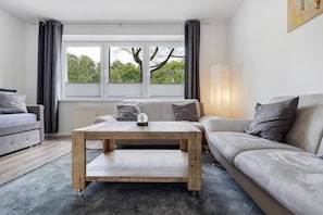 A modern living room with a sofa, a coffee table, and a view through a window.
