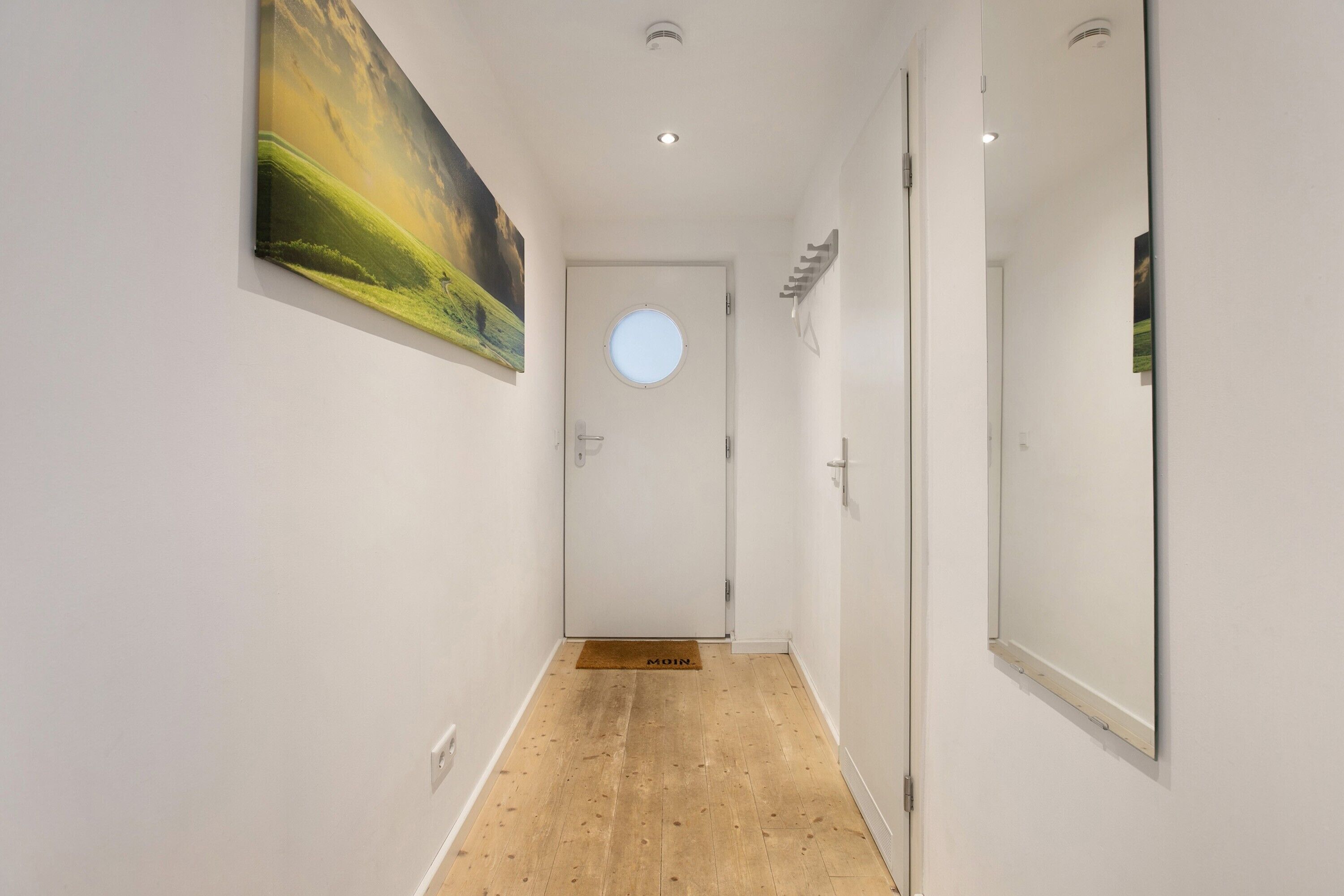 Ein Korridor mit Holzboden, einer runden Tür mit Fenster und einem Gemälde an der Wand.