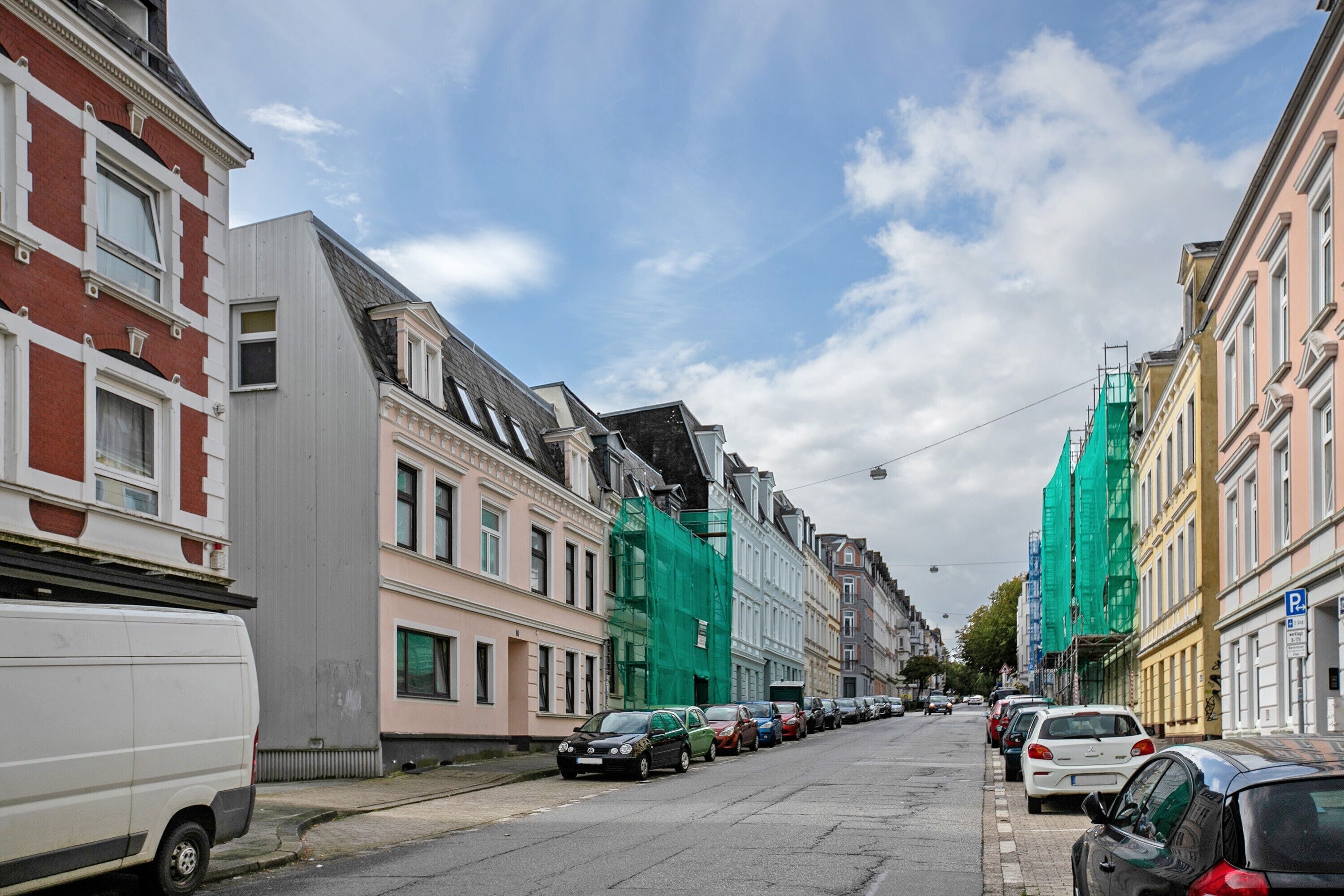 A street lined with multi-story buildings, parked cars, and a white van.