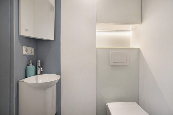 Un baño con un lavamanos blanco, un espejo, un interruptor de luz y un inodoro.