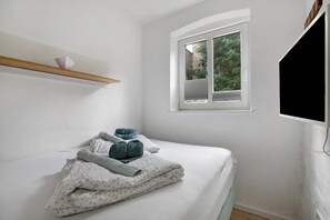 Makuuhuone, jossa on sänky, ikkuna, televisio ja hylly.