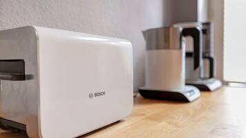 Un tostador blanco Bosch sobre una mesa de madera, junto a una cafetera de acero inoxidable.