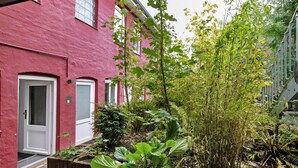 Een rood gebouw met een deur en ramen, omringd door groen en een kleine tuin.