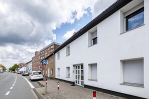 Eine Wohnstraße mit einem weißen Gebäude, einem parkenden Auto und blauem Himmel.