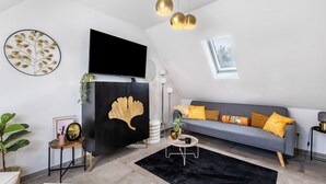 A modern living room with a flat-screen TV, a sofa with yellow cushions, a black accent wall, and a large window. - Apartment 'Deluxe' with Wi-Fi and Air Conditioning (Duisburg)