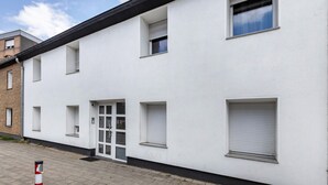 A white building with multiple windows, a door, and a small window with a view. - Apartment 'Deluxe' with Wi-Fi and Air Conditioning (Duisburg)