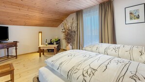 A room with wooden flooring, a bed with patterned bedding, a desk with a television, a vase with flowers, and a window with curtains. - Apartment 'Haus Kali' with Mountain View, Shared Terrace and Wi-Fi (Teisendorf)