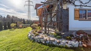 A house with a wooden structure, a garden with rocks and plants, and a power line tower in the background. - Apartment 'Haus Kali' with Mountain View, Shared Terrace and Wi-Fi (Teisendorf)