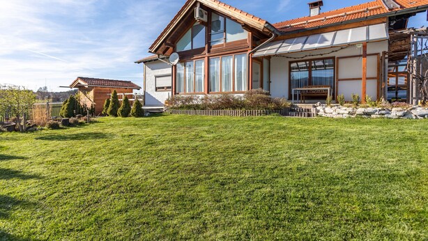 A two-story house with a sloped roof, large windows, and a well-maintained lawn. - Apartment 'Haus Kali' with Mountain View, Shared Terrace and Wi-Fi (Teisendorf)