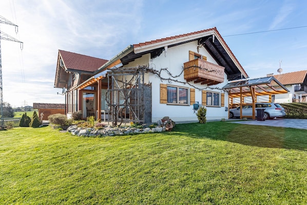 Une maison avec un toit en pente, un balcon en bois et une voiture garée dans l’allée.
